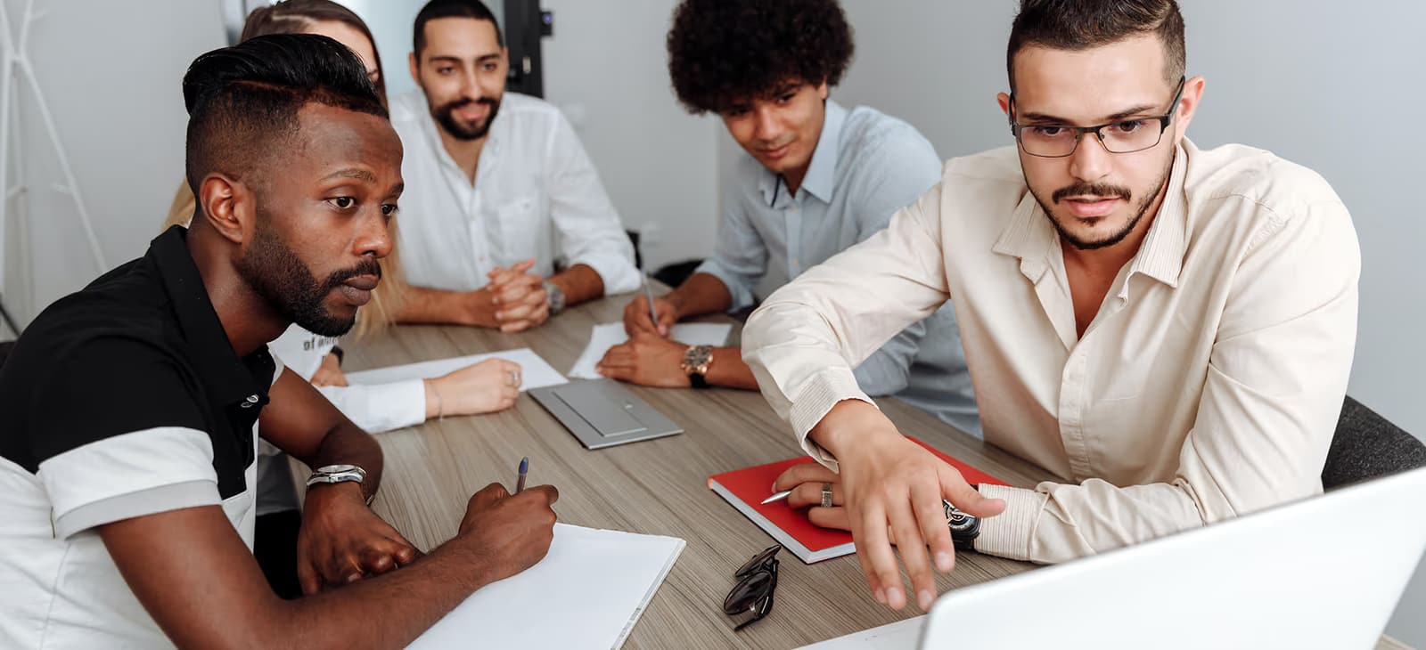 Senior lead pointing at a laptop while mentoring team members in a meeting