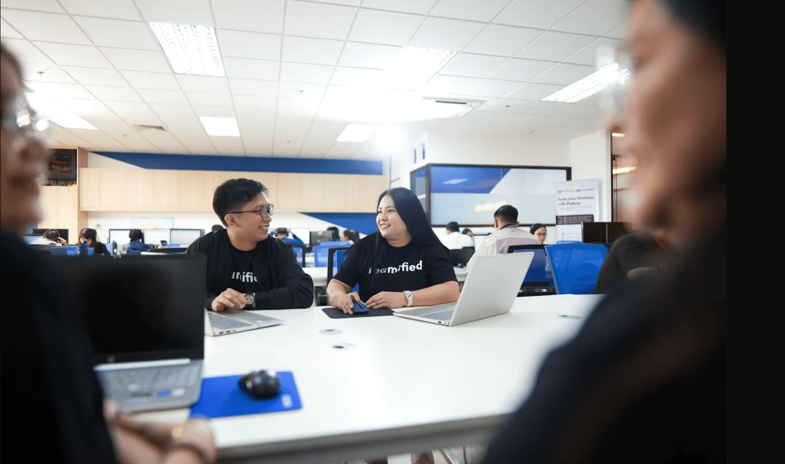 Two Teamified team members chatting at a shared desk in the office